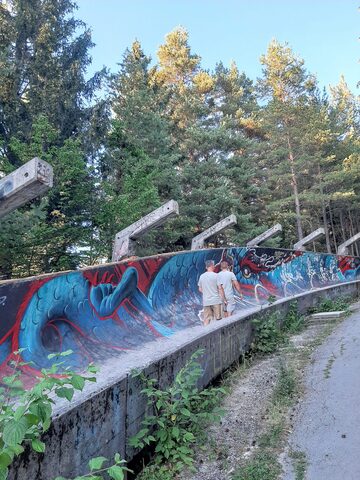 The Sarajevo bobsled track viewed along its length, concrete channel banking into a turn with pine forest closing in on both sides.