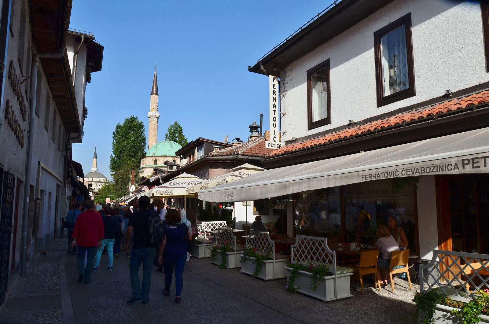 Bravadžiluk — a short cobbled lane in Baščaršija lined with low shopfronts and grill restaurants. The street is the canonical ćevapi address in Sarajevo.