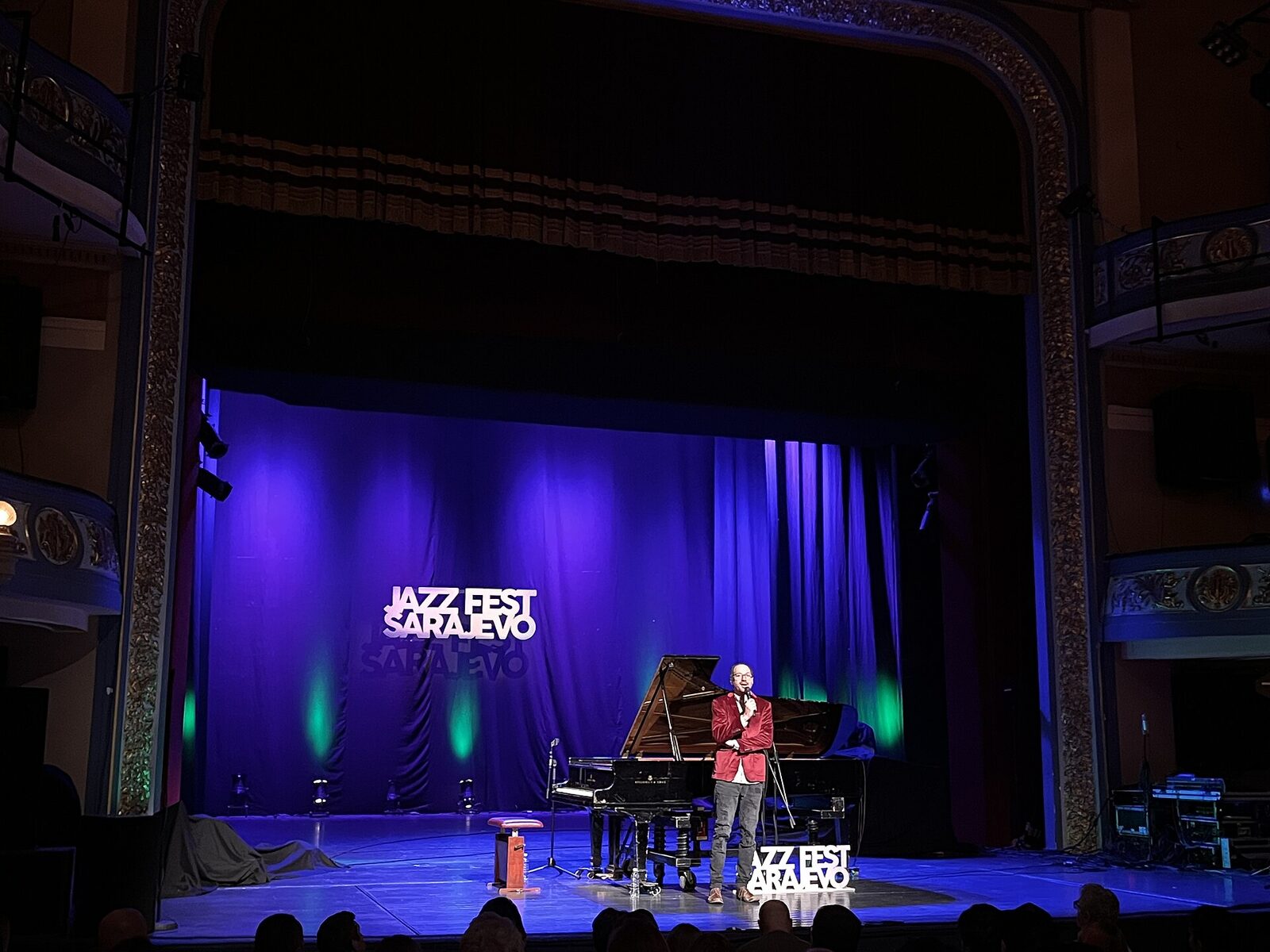 Jazz Fest Sarajevo stage at the National Theatre — grand piano under blue stage lights, the festival logo projected on the curtain.
