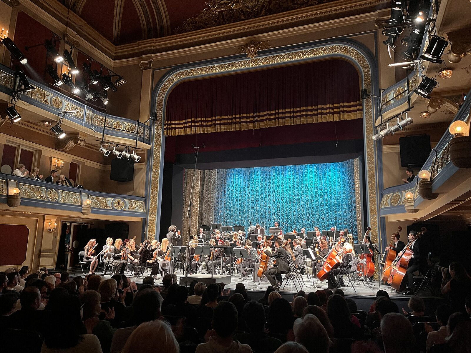 Interior of the National Theatre in Sarajevo — auditorium, proscenium arch, and stage with an orchestra performing under stage lights.
