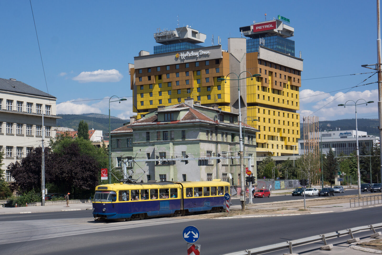 The yellow Holiday Inn hotel on Zmaja od Bosne in Sarajevo, designed by Ivan Štraus for the 1984 Winter Olympics — the building where the SDA was founded in 1990, where the SDS briefly headquartered, and from whose upper floors gunmen fired down at peace demonstrators on 6 April 1992.