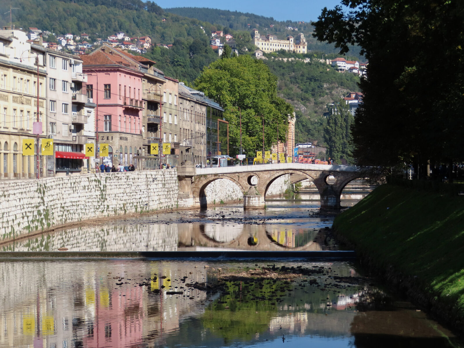 The Miljacka river and the Latin Bridge in Sarajevo, seen from the north bank. The corner just north of the bridge is where the Archduke Franz Ferdinand and his wife Sophie were shot on 28 June 1914 — the event that R.W. Seton-Watson made his four Yugoslav journeys to investigate.