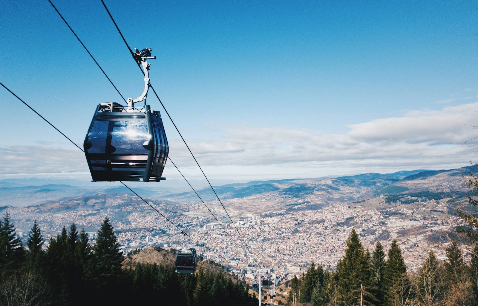 A red Trebević cable car cabin passing over the wooded slopes above Sarajevo.