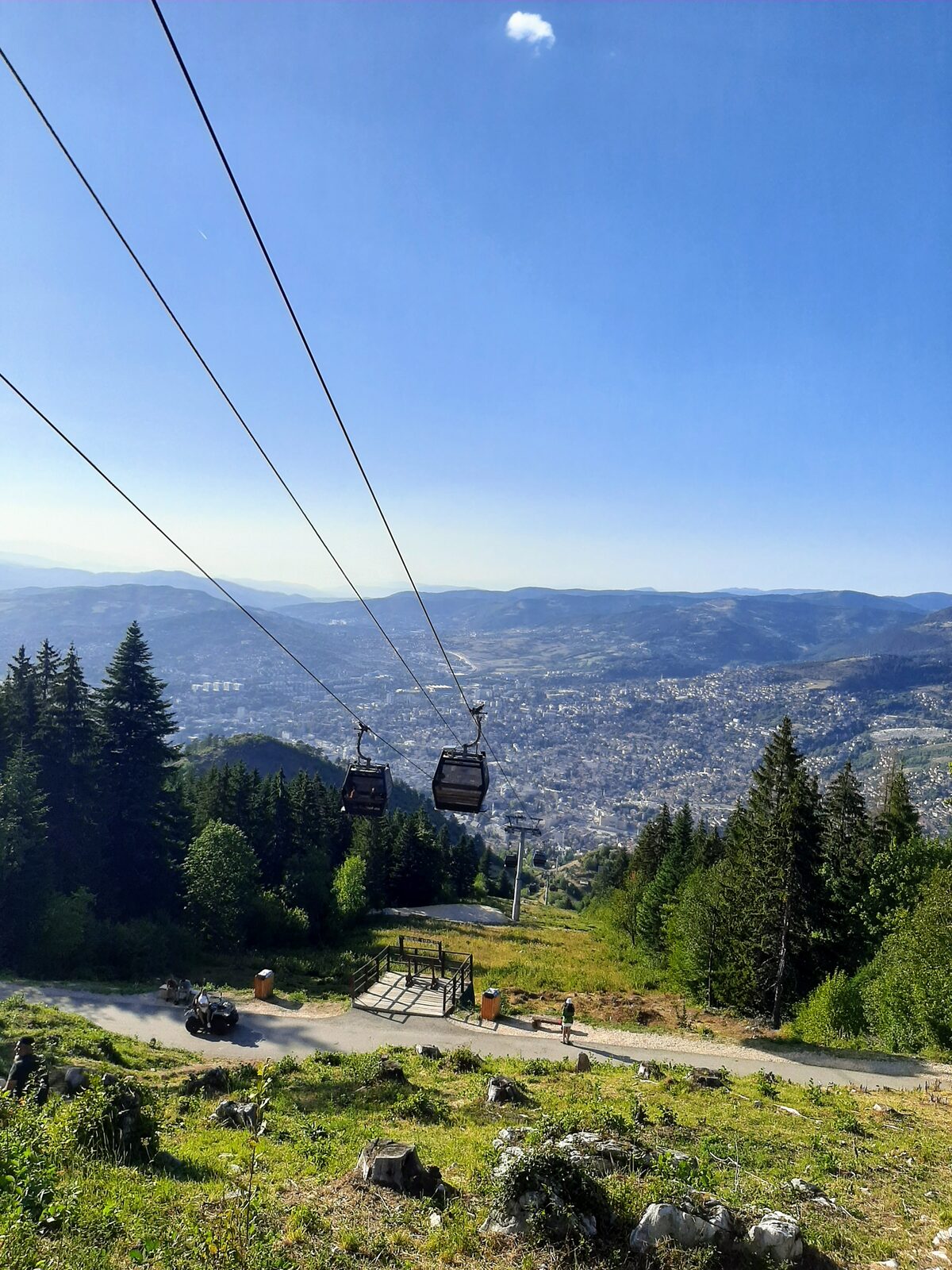 A Trebević cable-car cabin on the ascent above Bistrik, cable running up-slope, the Sarajevo valley visible below.