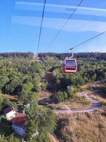 View through a cabin window of a red cabin passing below over forested slopes and a winding road.