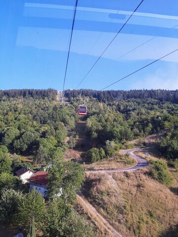 View from inside a cable car cabin of a red cabin passing below over the forest.