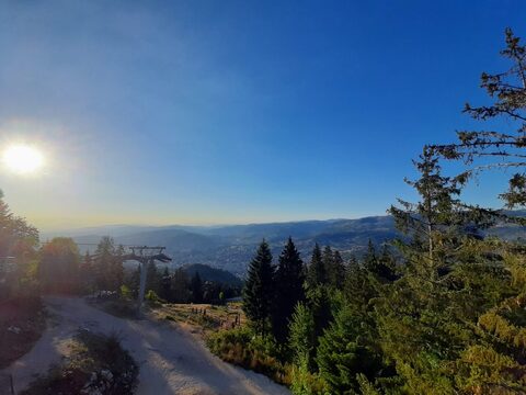 Late sun over the Trebević ridge path, a cable car pylon and the Sarajevo valley in haze below.