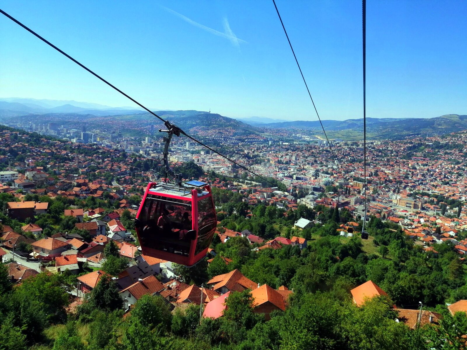 A Trebević cable car cabin crossing above the Bistrik neighbourhood with the city visible below.