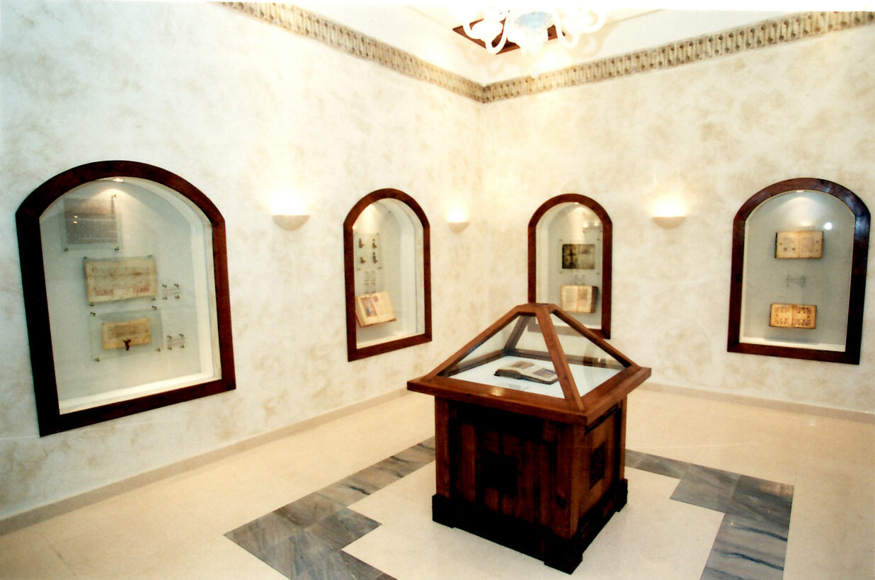 The vault room at the National Museum of Bosnia and Herzegovina photographed in December 2002 — a small, dimly lit chamber with a central display case for the Haggadah, flanked by glass cases holding Catholic, Orthodox, and Muslim manuscripts.