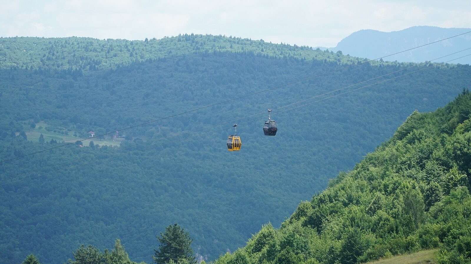 The rebuilt Trebević cable car in Sarajevo, a modern gondola cabin suspended on cables above the city, with the Sarajevo valley and mountains visible below.