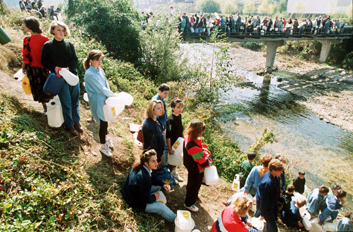 Civilians queuing with plastic canisters and jerrycans for drinking water in besieged Sarajevo in 1992 — one of the water lines that the Sarajevska Pivara brewery well supplied through the siege.