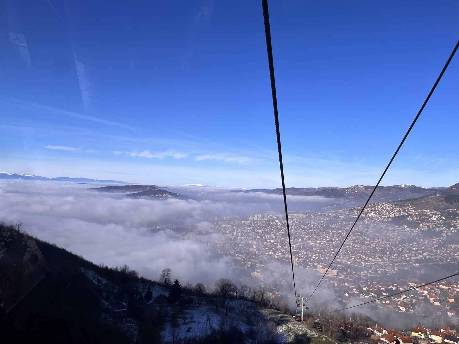 A panoramic view from the upper ridge of Trebević in winter, with the city of Sarajevo laid out below in the valley.