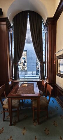 A small wooden table for four set in a tall arched window with heavy fringed curtains drawn back to the street.
