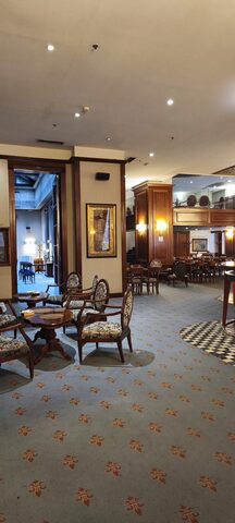 Upholstered armchairs around small round wooden tables on a blue carpet patterned with fleur-de-lis.