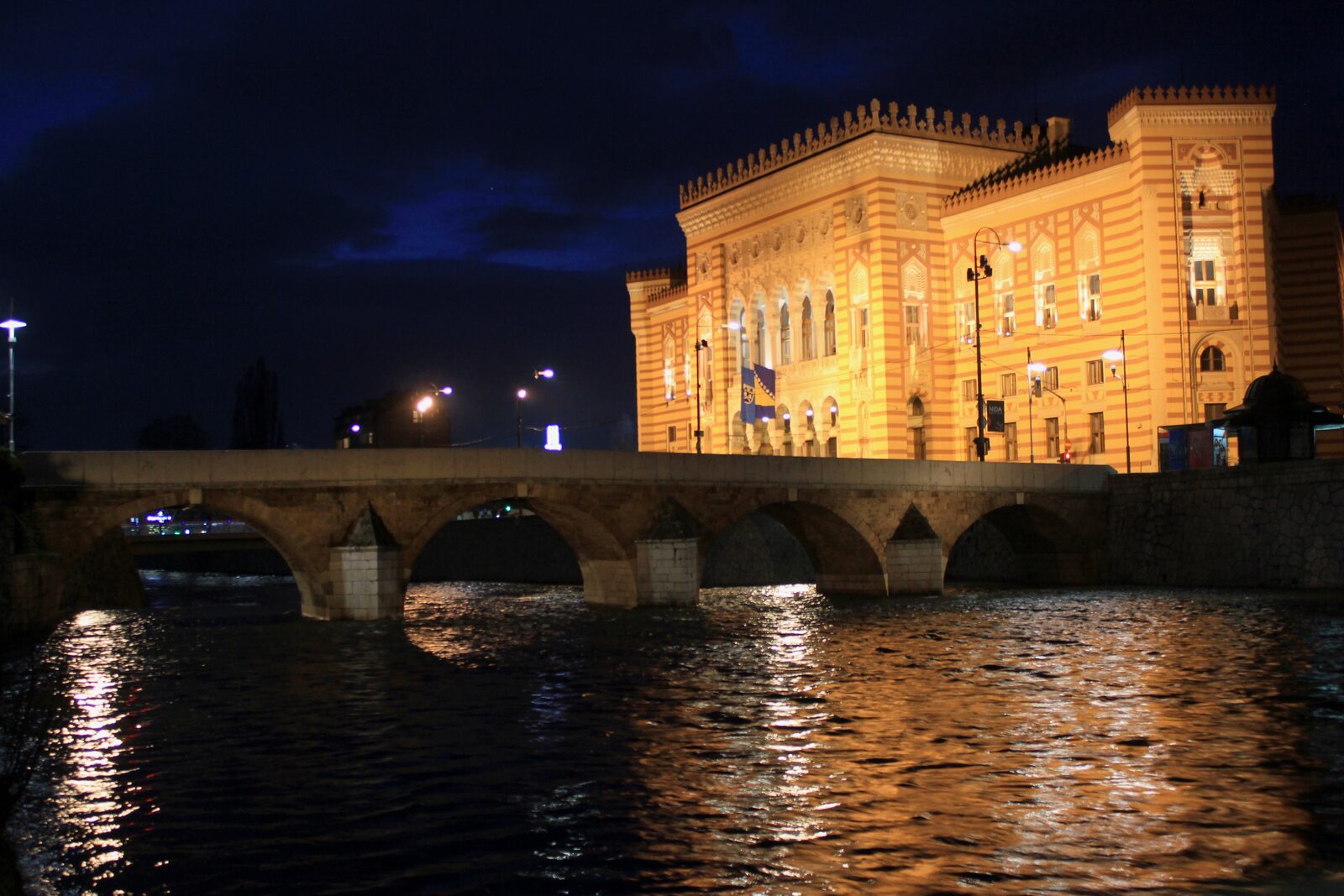 The Sarajevo City Hall (Vijećnica), a late-19th-century Pseudo-Moorish building on the Miljacka, with its striped sandstone façade, horseshoe arches, and central glazed atrium.