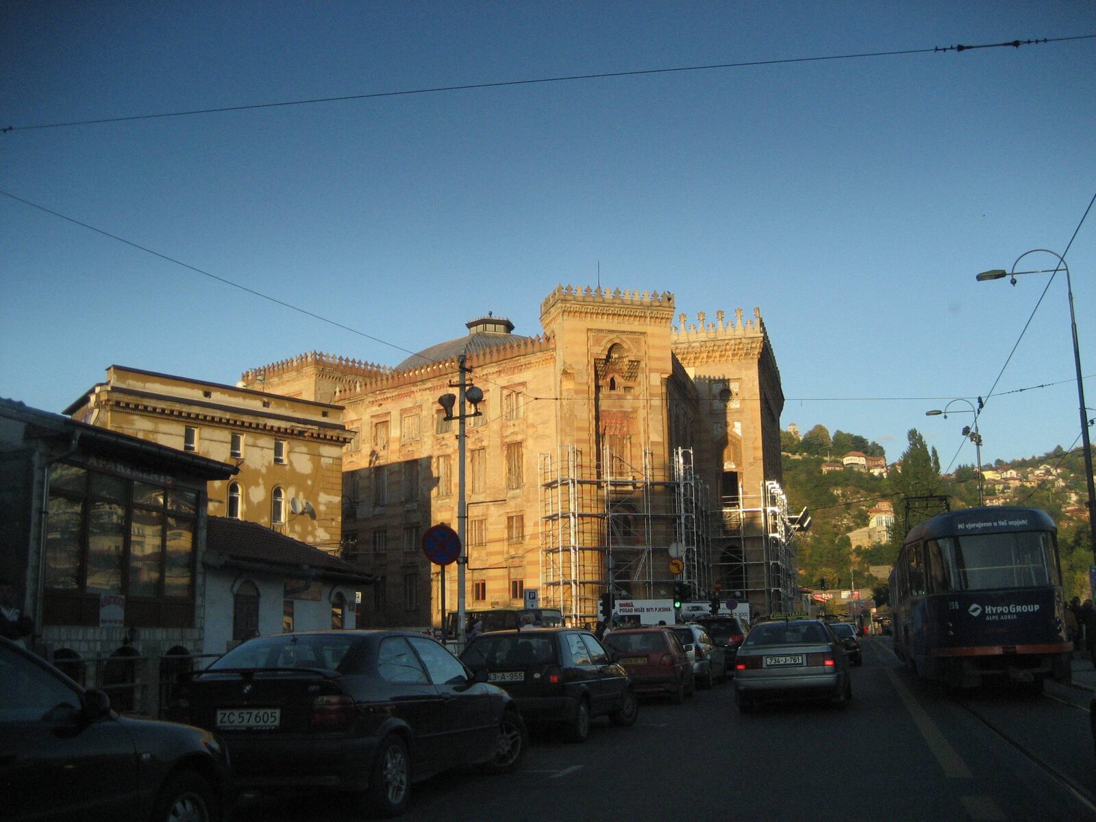 Vijećnica's striped pseudo-Moorish façade by day, with a tram passing in the foreground.
