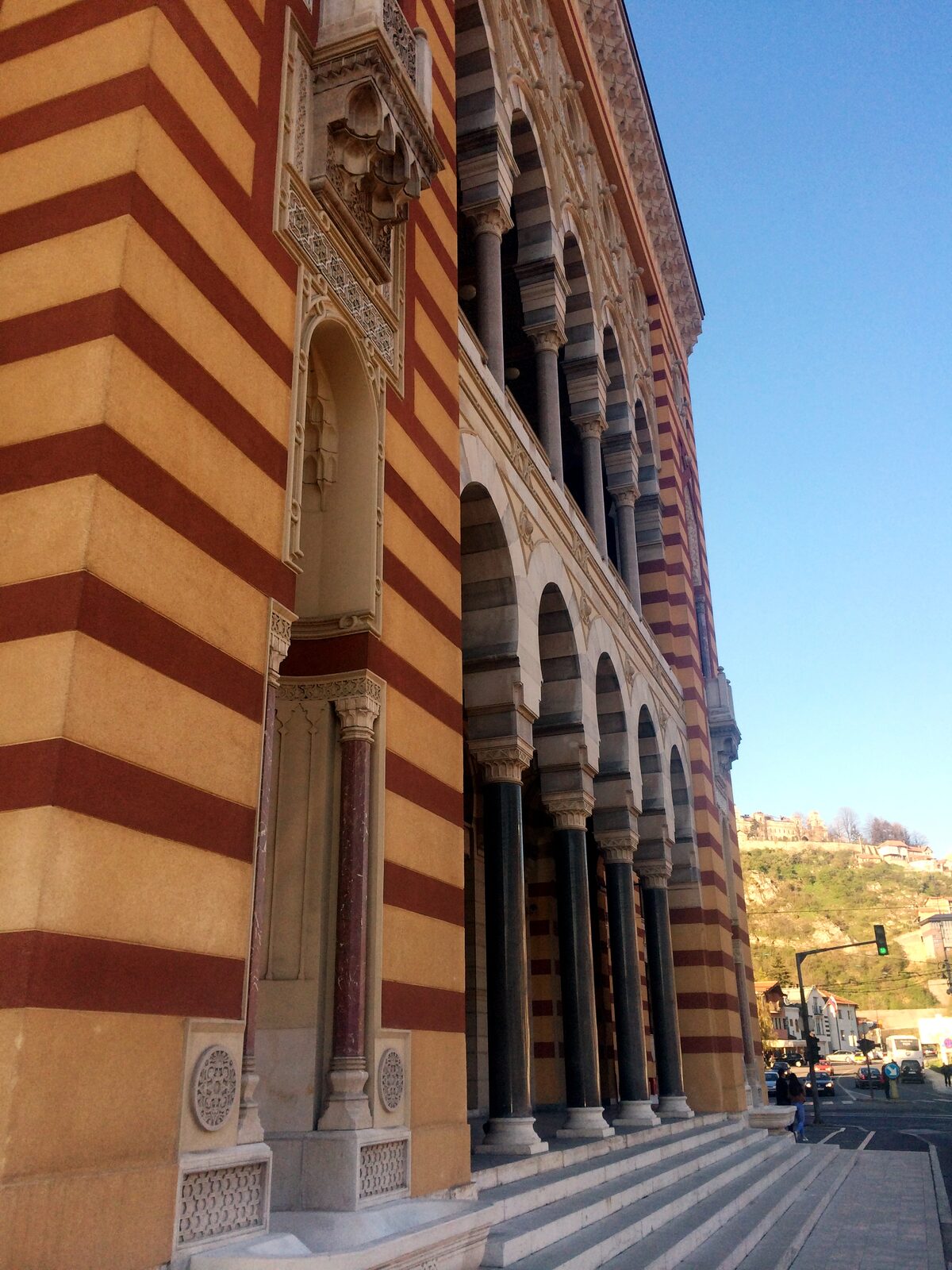 An interior arcade of Sarajevo's Vijećnica, the striped Habsburg-Moorish arches and painted upper walls — the kind of library-adjacent interior Kemal Bakaršić spent his working life in, before the siege put it under artillery.