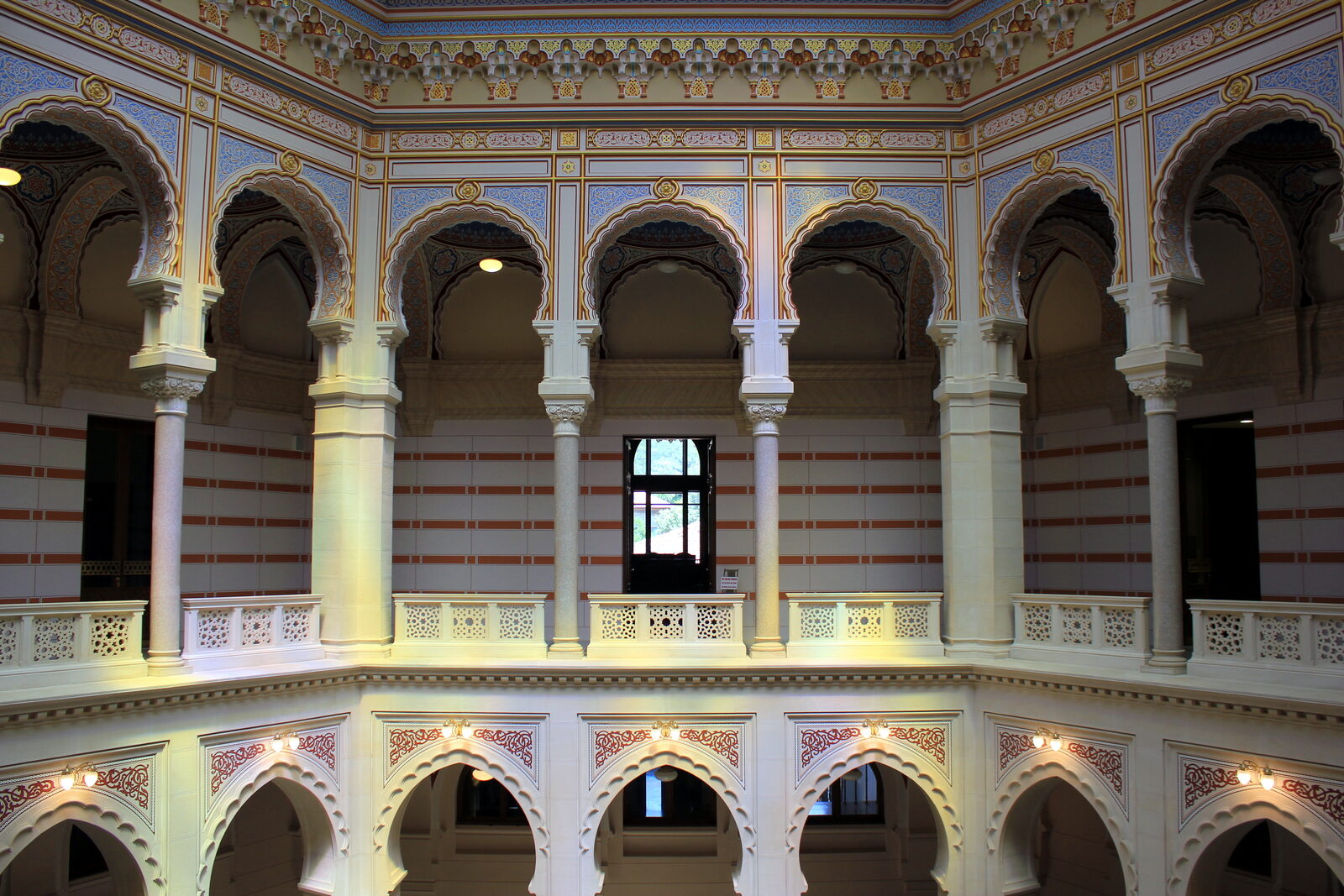 The central rotunda of the Sarajevo Vijećnica after restoration — banded stone arches rising to the stained-glass dome, the equilateral-triangle plan Pařík drew in August 1892 legible in three dimensions.